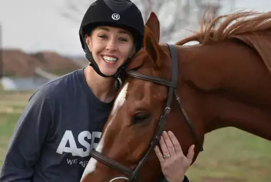 woman in helmet hugs her horse