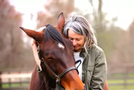 a woman stands next to a brown horse hugging him around his neck sweetly