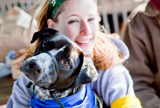woman holds dog wearing a blue bandana outdoors smiling