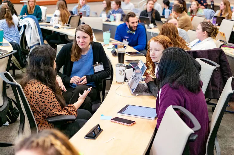 Veterinary students sit at a desk in a large room learning various animal techniques