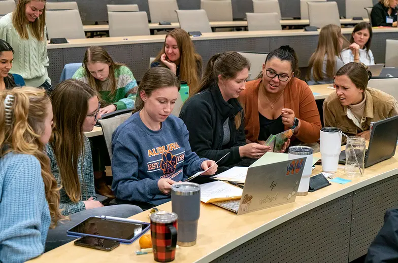 Veterinary students sit at a desk in a large room learning various animal techniques